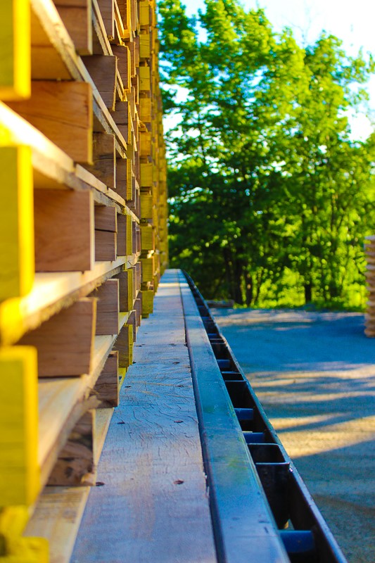 Stack of freshly painted yellow wooden pallets loaded onto a truck at Troymill with green trees in the background.